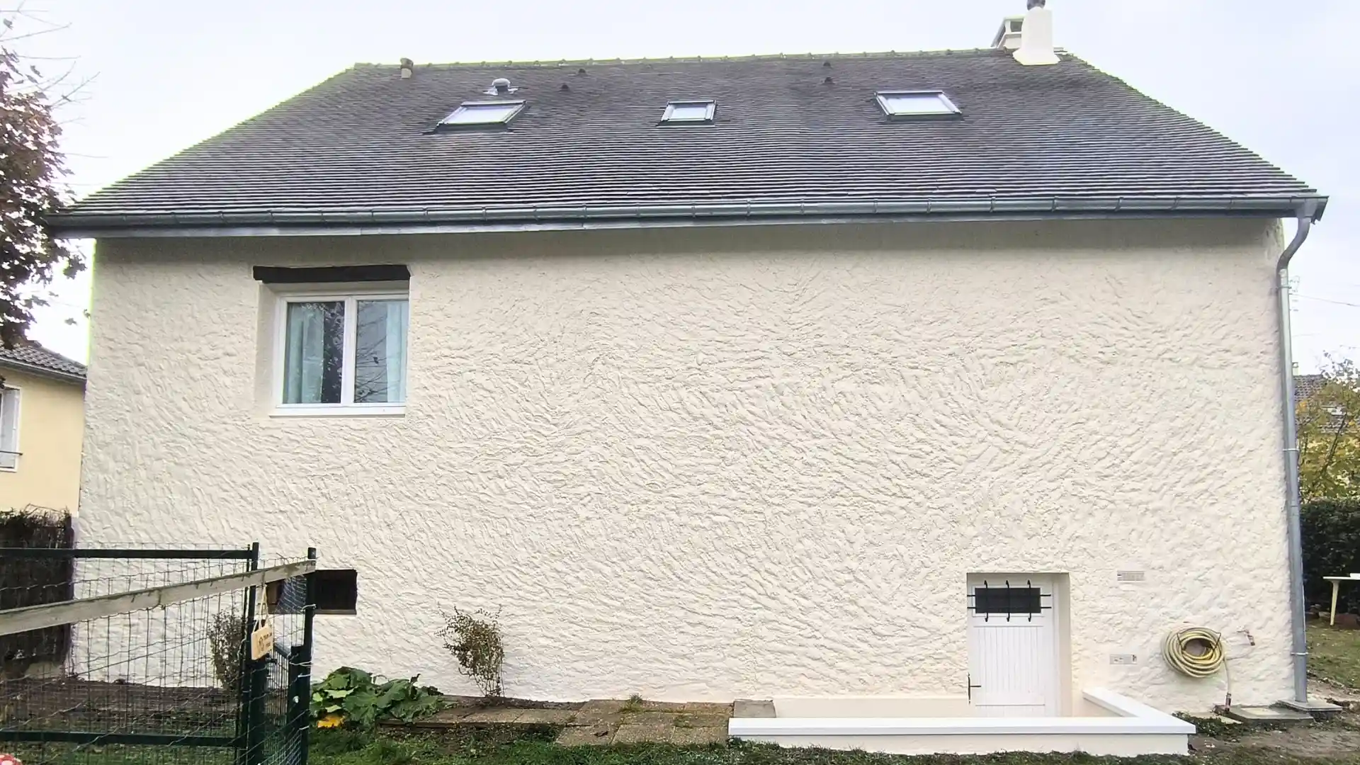 Façade arrière de la maison après travaux de ravalement, présentant un nouvel enduit blanc propre, une porte d'entrée blanche et deux fenêtres de toit