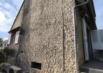 Vue verticale d'un pignon de la maison avant les travaux, illustrant l'état dégradé et sale de l'ancien enduit de façade.