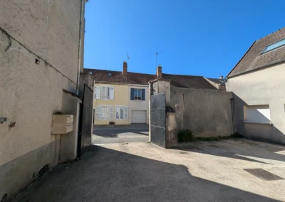 Vue depuis la cour vers la rue a Ablis avant travaux, montrant un portail et des murs de cloture a lenduit encrasse et vieilli