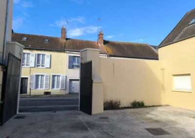 Vue depuis la cour vers la rue apres travaux, mettant en valeur le nouveau ravalement lumineux et les poteaux de portail repares avec la solution I4S
